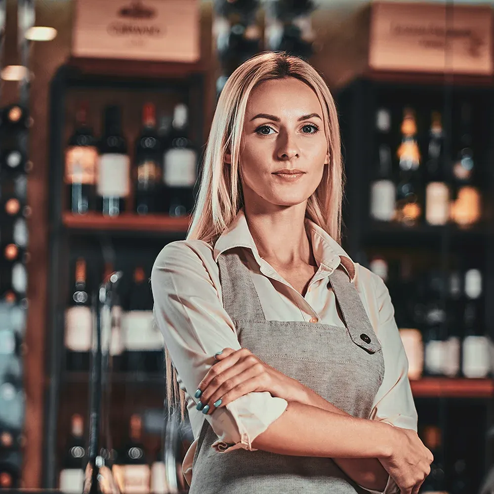 A woman with folded arms stands in front of a bar