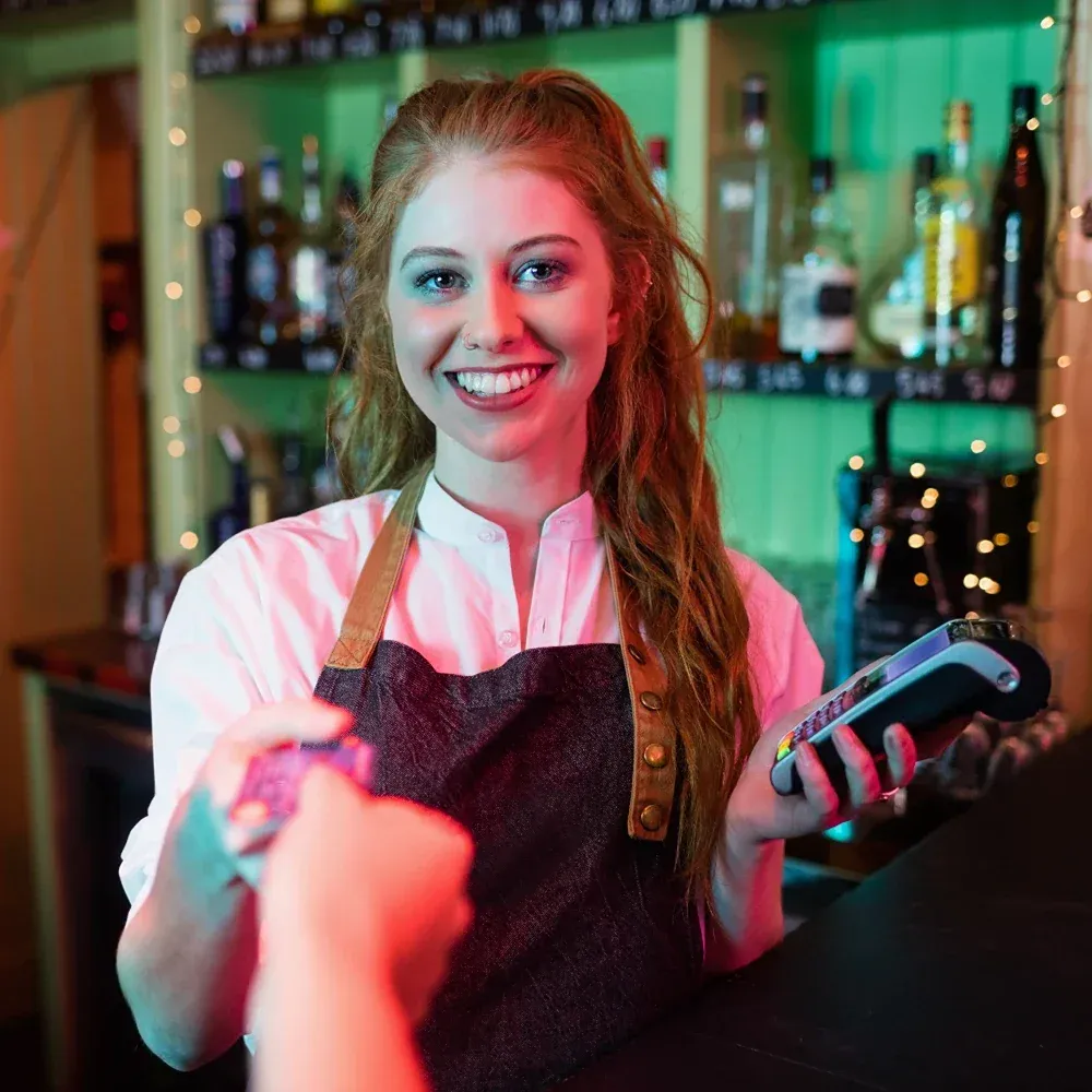 A smiling female bar worker taking a payment from a customer